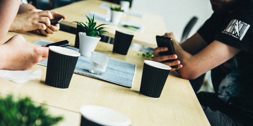 Personer runt ett bord med kaffekoppar och mobiler
